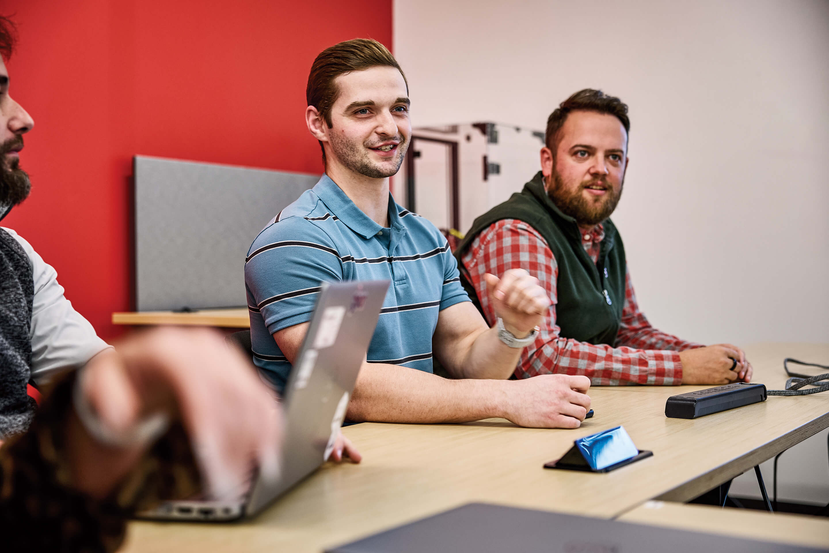Three men at a table with laptops, focused on their work and sharing ideas in a collaborative setting.