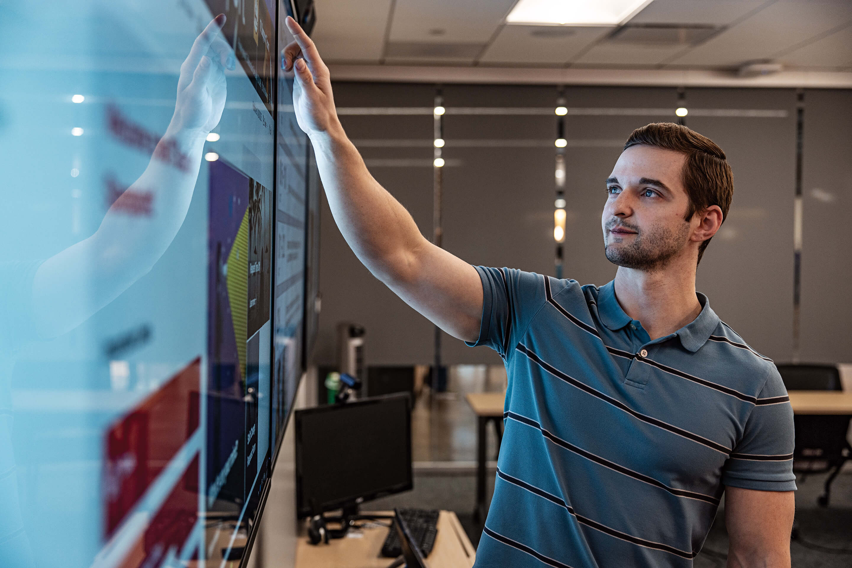 A man points at a large screen in an office setting, indicating key information or visuals.