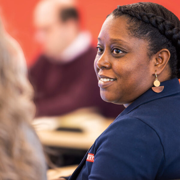 A woman in a blue jacket is seated at a table, appearing focused and thoughtful.
